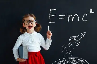 Child girl prodigy student with book near blackboard